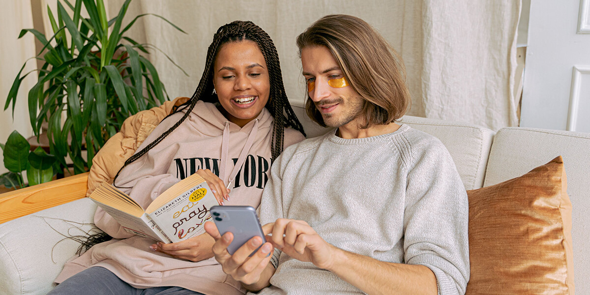 A couple sits looking at a phone as a woman holds a book in her hands. 3D rendering, design studio, 3D product, animation, character design, 2D animation, video production services, book trailer services, digital marketing services, motion design, motion graphics. RDV Media – Multimedia production company. Serving brands globally. New York, Los Angeles, California, Atlanta, USA, Dublin, Ireland, EU, London, England, UK, Doha, Qatar, UAE, Abu Dhabi, Ajman, Dubai, Fujairah, Ras Al Khaimah, Sharjah, and Umm Al Quwain.