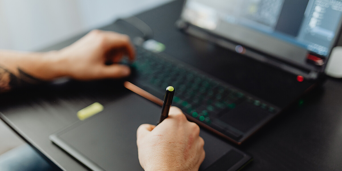 Person using a stylus on a digital drawing tablet with a keyboard and laptop visible in the background. 3D rendering, design studio, 3D product, animation, character design, 2D animation, video production services, book trailer services, digital marketing services, motion design, motion graphics. RDV Media – Multimedia production company. Serving brands globally. New York, Los Angeles, California, Atlanta, USA, Dublin, Ireland, EU, London, England, UK, Doha, Qatar, UAE, Abu Dhabi, Ajman, Dubai, Fujairah, Ras Al Khaimah, Sharjah, and Umm Al Quwain.