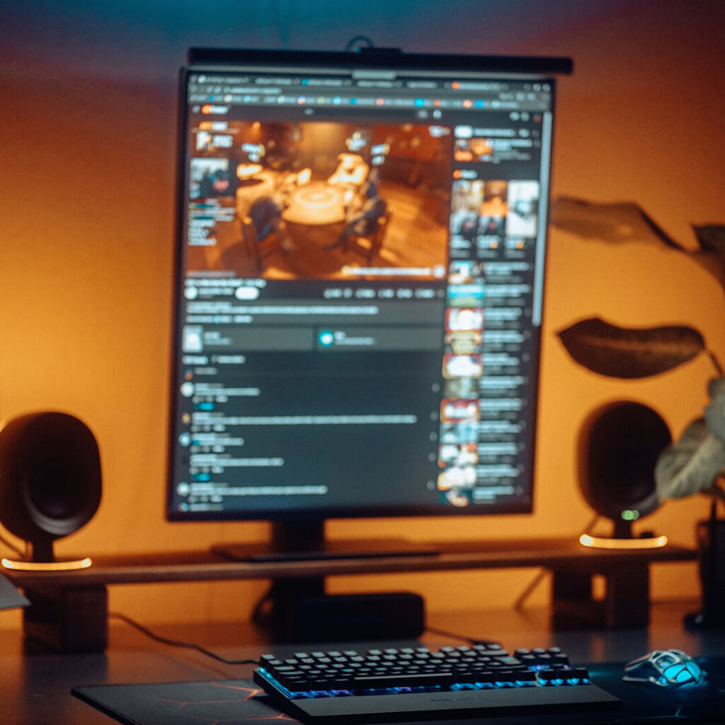 A YouTube livestream setup with a vertical monitor displaying an active stream, colorful ambient lighting, speakers, and a keyboard on a wooden desk. RDV Media – Multimedia production company. Serving brands globally.