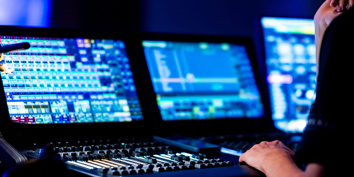 Audio engineer working at a sound mixing console with multiple monitors displaying audio editing software in a recording studio. RDV Media – multimedia production and marketing company. Serving brands globally.